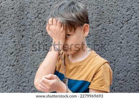 Portrait of a 10-year-old criminal, a boy handcuffed against a gray wall. Concept: juvenile delinquency, petty theft and theft, incarceration. Royalty-Free Stock Photo #2279969693