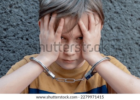 A juvenile delinquent in handcuffs against a gray wall, close-up. Concept: juvenile delinquency, petty theft and theft, incarceration. Royalty-Free Stock Photo #2279971415