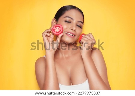 Beautiful Young Asian woman natural and fresh skin face applying tomato slices for spa treatment and skin care isolated on yellow wall.