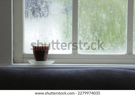 A glass of black coffee on the Window Sill, with against the warm light from the sunny day outside. Royalty-Free Stock Photo #2279974035