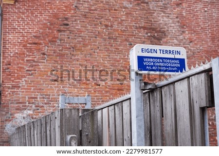 Dutch blue private property sign with in the background a stone wall and a fence with barbed wire. Translation: Private property, Authorized access only