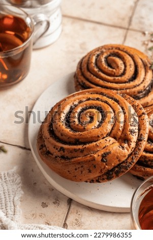 Twisted buns with poppy seeds for morning breakfast tea on beige tile background close up. Swirl brioche with poppy seeds. Vertical orientation