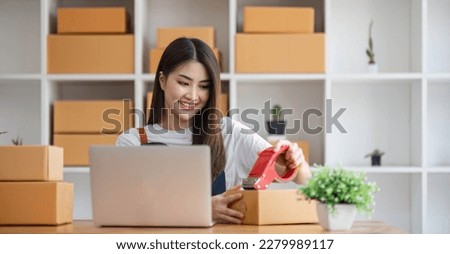 A portrait of a young Asian woman, e-commerce employee sitting in the office full of packages in the background write note of orders and a calculator, for SME business ecommerce and delivery business.