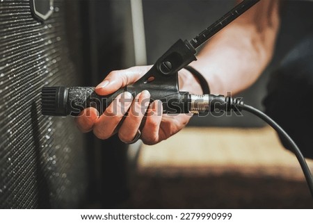 Male hand with long nails positioning dynamic microphone on electric guitar cabinet inside recording studio, sound engineer at work