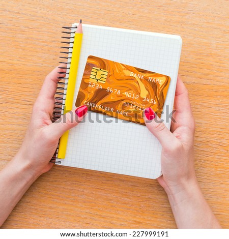 Woman hand holding notebook and credit card on wooden background