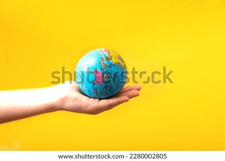 Child hand holding globe in a hands on yellow background. World Earth Day concept. Green Energy, renewable and sustainable resources. Protecting and save planet.
