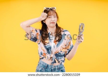 A woman with a hawaiian shirt and holds a portable fan and wipes her eyes.