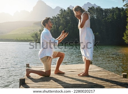 Man, woman and marriage proposal by lake on vacation with surprise, wow or happiness in sunshine. Couple, engagement and offer ring in nature for romance, love and happy on holiday in summer by water Royalty-Free Stock Photo #2280020217