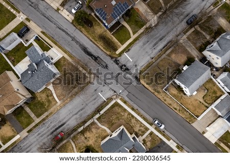 An aerial, top down view directly over a residential neighborhood on Long Island, New York during a cloudy day. Centered over a road intersection, showing similar middle-class houses.