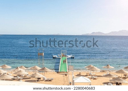 Luxury beach against the background of the beauty of the sea with coral reefs. Nice beach with beach chairs, thatched umbrellas and palm trees. 