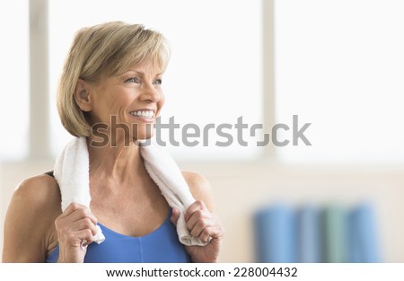 Happy mature woman with towel around neck looking away at home Royalty-Free Stock Photo #228004432