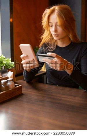 Young woman making card payment through mobile phone to pay bills. Vertical photo.