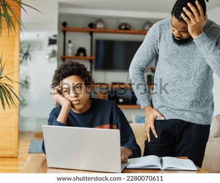 Father and son doing homework with laptop fighting and arguing over learning at home. Father and teenage son using laptop. Boy and dad sitting at home working with notebook, boy being bored Royalty-Free Stock Photo #2280070611