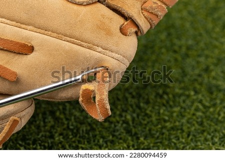 Repairing baseball glove laces with lacing needle. Glove relacing, sports equipment repair and maintenance concept. Royalty-Free Stock Photo #2280094459