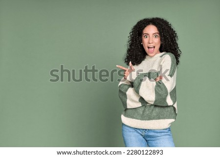 Young excited surprised latin woman pointing fingers aside isolated on green background. Amazed female model showing advertising great choice presenting sale offer promotion crazy discounts concept. Royalty-Free Stock Photo #2280122893
