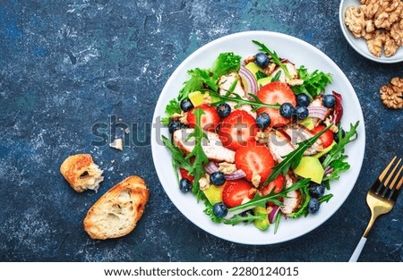 Strawberry, grilled chicken and herbs healthy salad with arugula, blueberries, avocado and walnuts, blue kitchen table. Fresh useful dish for healthy eating Royalty-Free Stock Photo #2280124015