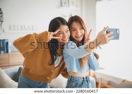 Two asian young women happy smiling and taking selfie in living room at home. Video call, Meeting conference Royalty-Free Stock Photo #2280160417