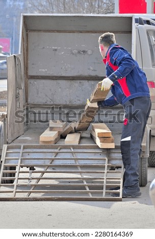 A man loads wooden planks into a trailer on a spring day