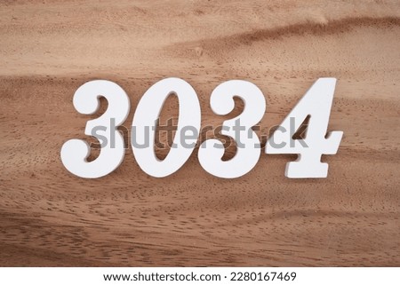 White number 3034 on a brown and light brown wooden background.

