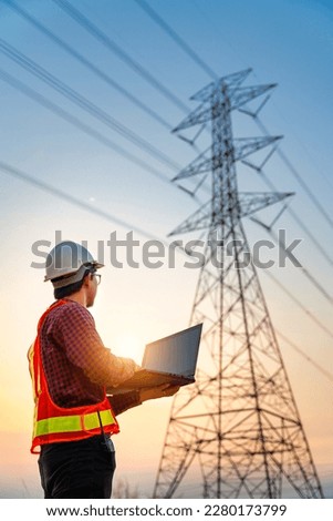 Asian electrical engineers checking location using a notebook computer standing at a power station to view the planning work by producing electrical energy at high voltage electrodes. Vertical image. Royalty-Free Stock Photo #2280173799
