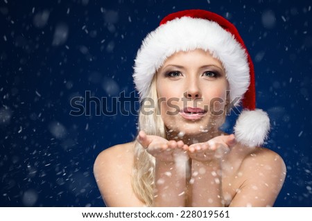 Attractive woman in Christmas cap blows kiss, winter background