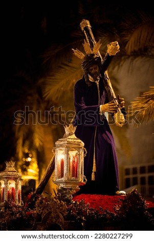 Throne with red flowers and candle lanterns of Jesus of Great Power carrying the penitential cross during the Andalusian Holy Week.