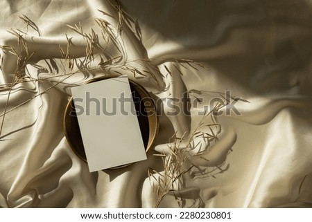 Blank paper sheet card with mockup copy space on crumpled glossy gold silk cloth background with sunlight shadows silhouette. Aesthetic bohemian minimal business brand template. Flat lay, top view