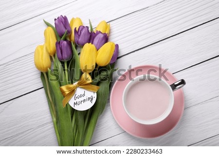 Cup of hot drink, beautiful tulips and card with text Good Morning on white wooden table, flat lay