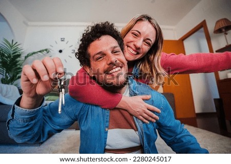 Young caucasian couple showing keys of their first house after purchase and moving to new home together. happy husband and wife hugging in their apartment excited to be owners of a apartment. High Royalty-Free Stock Photo #2280245017