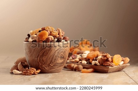 Dried fruits and nuts on a beige ceramic table. The mix of nuts, apricots, and raisins in a wooden bowl. Copy space. Royalty-Free Stock Photo #2280245999