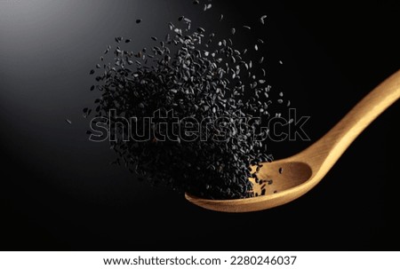 Grains of black sesame is poured with a wooden spoon. Black sesame on a dark background. Copy space. Royalty-Free Stock Photo #2280246037