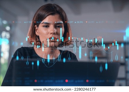 Pensive attractive beautiful businesswoman in formal wear working on laptop at office workplace in background. Forex graph and charts hologram icons. Concept of market trading and research.