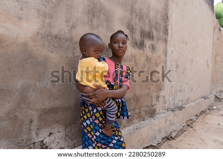 Underage African mother carrying her baby boy on her arms; concept of early marriage and motherhood Royalty-Free Stock Photo #2280250289