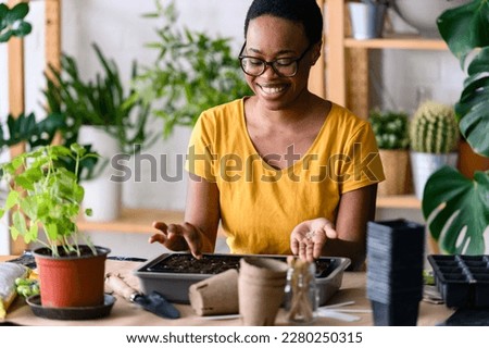 Young smiling african-american woman doing seed-starting early in the spring indoors for her backyard garden or a homestead garden Royalty-Free Stock Photo #2280250315