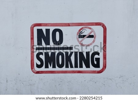 No smoking sign with a crossed out cigarette in a red square painted on a white wall