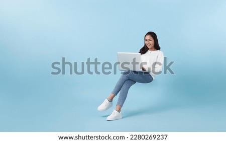 Young smiling Asian girl student floating in mid-air with using laptop isolated on blue studio copy space background. Royalty-Free Stock Photo #2280269237