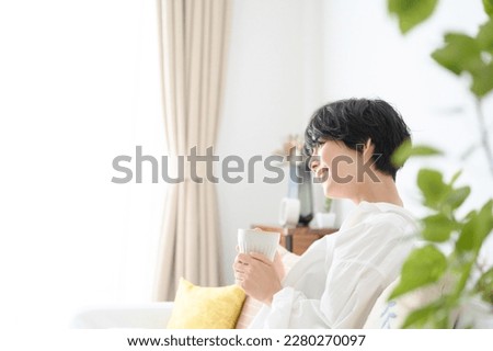An Asian woman relaxes with a drink and a smile. Royalty-Free Stock Photo #2280270097