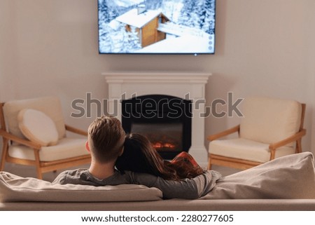 Lovely couple spending time together on sofa near fireplace at home, back view