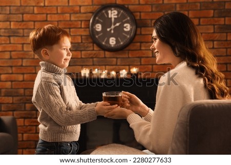 Mother and son with cup of tea near fireplace at home