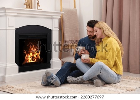 Lovely couple with hot drinks spending time together near fireplace at home