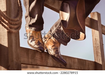 Cowboy boots and hat sitting on fence at ranch rodeo with feet up resting, country music festival live concert or line dancing concept