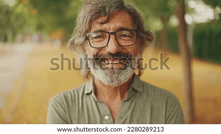 Clouse-up, friendly middle-aged man with gray hair and beard wearing casual clothes looks at the camera. Mature gentleman in eyeglasses smiles at the camera Royalty-Free Stock Photo #2280289213