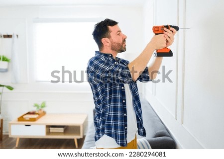 Attractive handy man using a drill to put up pictures and decorations on the wall after moving to a new house