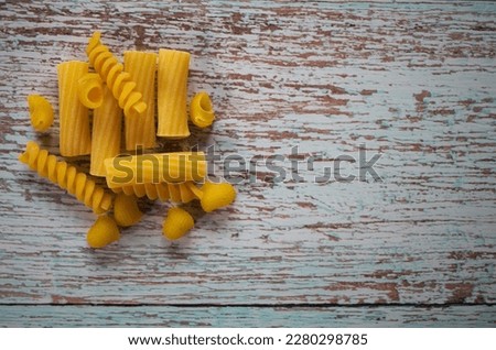 A horizontal food photo of a pile of different type of uncooked pasta on a wooden table. An image with copy paste space on the right.