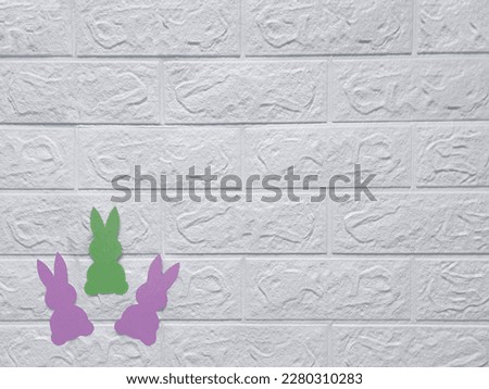 Crafts for preschoolers. Copy space. Happy Easter concept. Top view.  Colorful paper cutout rabbits on background of white wall. Flat lay. Place for text. Preparing for holiday, decorating house.