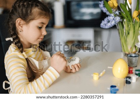 Happy little girl painting easter eggs on kitchen. Cute smiled girl have fun on spring holiday 