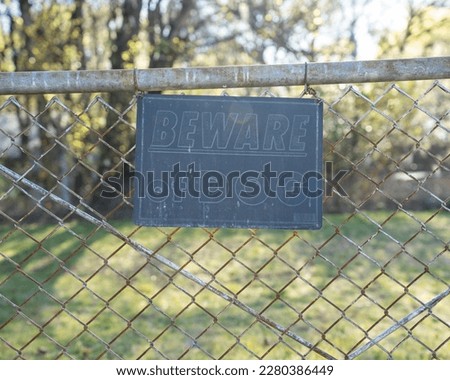beware of dog sign hanging on a chain link fence, warning sign sun worn sign battered sign