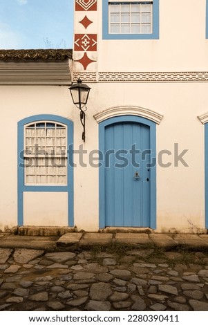 Paraty, Brazil. Facade of a colonial house from 1836 in white and blue colors. Door, window and old street lamp. Background blue sky. Royalty-Free Stock Photo #2280390411