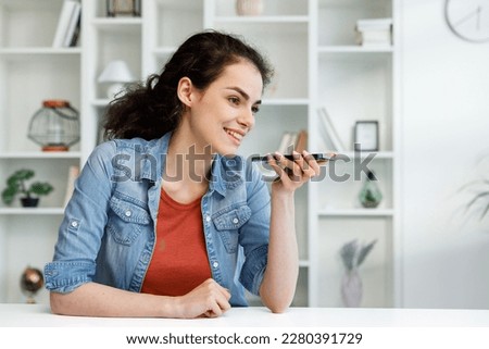Young curly brunette sitting at the table uses a mobile phone. A voice message. Surfs the Internet, communicates in instant messengers on his smartphone. Online communication, smartphone in human life Royalty-Free Stock Photo #2280391729