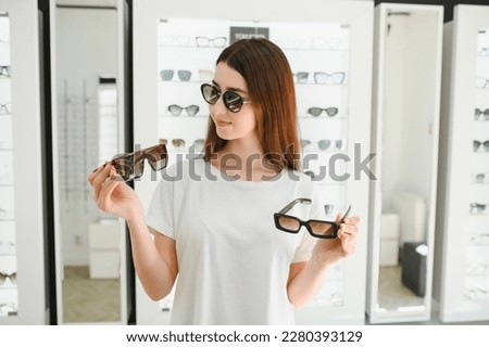Portrait of a young woman shopping, standing in store and trying sunglasses near a mirror Royalty-Free Stock Photo #2280393129
